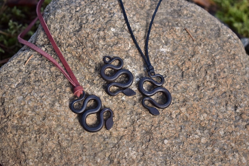 May include: Three black snake pendant necklaces on a rock background. The necklaces are made of wood and have a simple, elegant design. The pendants are all different sizes and shapes.