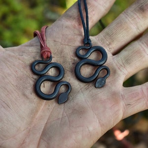 May include: Two black snake pendant necklaces on a hand. One necklace has a red cord and the other has a black cord.
