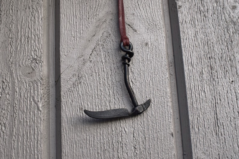 May include: A black metal hook with a brown leather cord hanging on a white wooden wall.