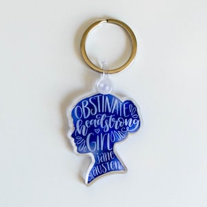May include: A blue and white keychain with a silhouette of a woman's head and the text "Obstinate headstrong girl Jane Austen".