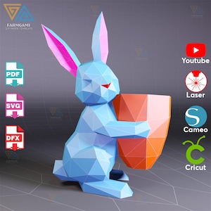 May include: A geometric papercraft bunny in light blue, holding an orange container. The bunny has pink inner ears and a red nose. The image includes icons for PDF, SVG, and DFX files, along with YouTube, Laser, Cameo, and Cricut logos.