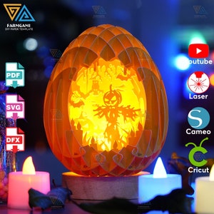 May include: A 3D papercraft model of a pumpkin with a jack-o'-lantern face and a scarecrow inside. The model is lit from within, creating a warm glow. The model is made of orange paper and is decorated with black and white details. The model is on a wooden base and is surrounded by candles.
