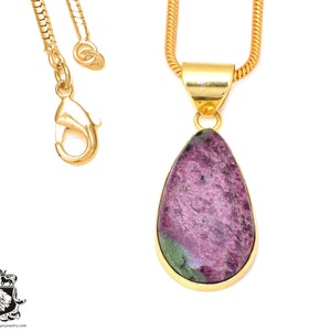 May include: A gold chain necklace with a teardrop-shaped pendant featuring a pink and green gemstone.