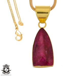 May include: A gold chain necklace with a pendant featuring a large, faceted, deep red ruby gemstone.