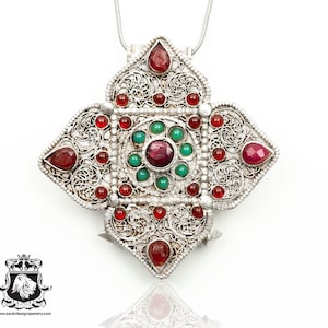 May include: A silver pendant with a filigree design and red and green gemstones. The pendant is in the shape of a cross and is attached to a silver chain.