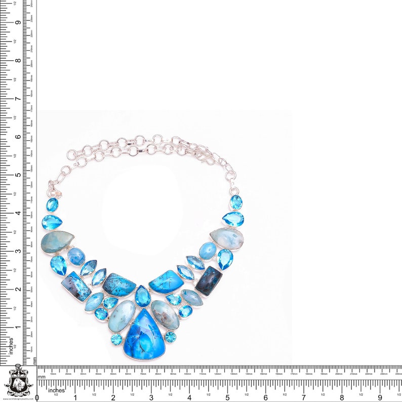 Puede incluir: Un collar de plata con un dise&ntilde;o en forma de V adornado con una variedad de piedras preciosas azules, incluyendo aguamarina, topacio y turquesa.