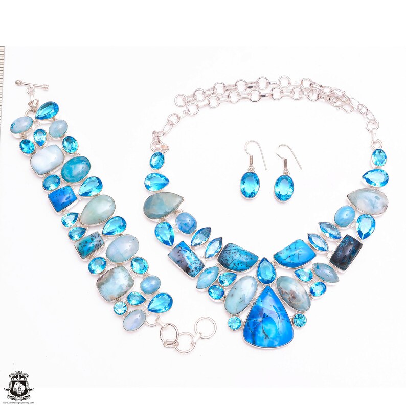 Puede incluir: Un conjunto de collar, pulsera y pendientes de plata con piedras preciosas azules y azul claro. El collar es una pieza llamativa con una gran piedra preciosa en forma de l&aacute;grima en el centro.