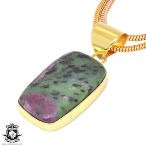 May include: A gold chain necklace with a rectangular pendant featuring a green and pink gemstone.