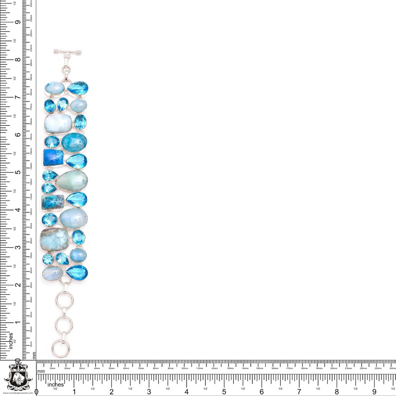 Puede incluir: Un brazalete de plata con una fila de piedras preciosas azules y azul claro. El brazalete mide aproximadamente 18 cm de largo y tiene un cierre de langosta.