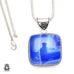 May include: A silver chain necklace with a square pendant featuring a blue agate stone. The pendant has an ornate silver design around the edge.
