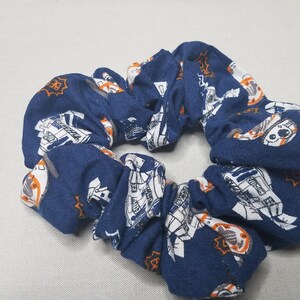 May include: A blue scrunchie with a white and orange pattern of a robot character.