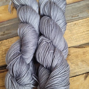 May include: Two skeins of grey yarn, wound into balls, on a wooden surface.