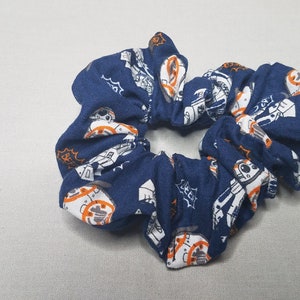 Op de afbeelding: Een blauwe scrunchie met een witte en oranje print van een robotpersonage.
