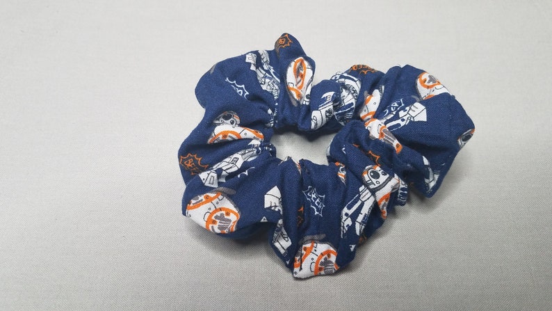 Op de afbeelding: Een blauwe scrunchie met een witte en oranje print van een robotpersonage.