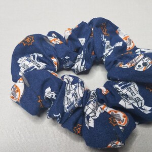 Op de afbeelding: Een blauwe scrunchie met een witte en oranje print van een robot.