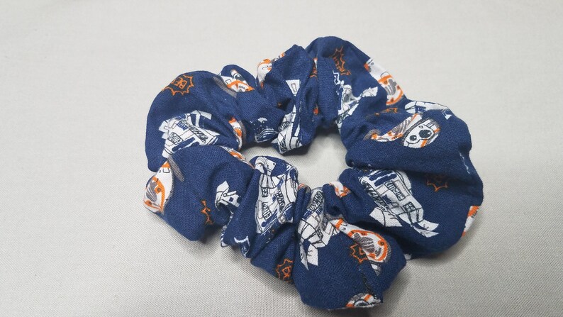 Op de afbeelding: Een blauwe scrunchie met een witte en oranje print van een robot.