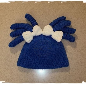 May include: A blue crocheted hat with two white crocheted bows on top.