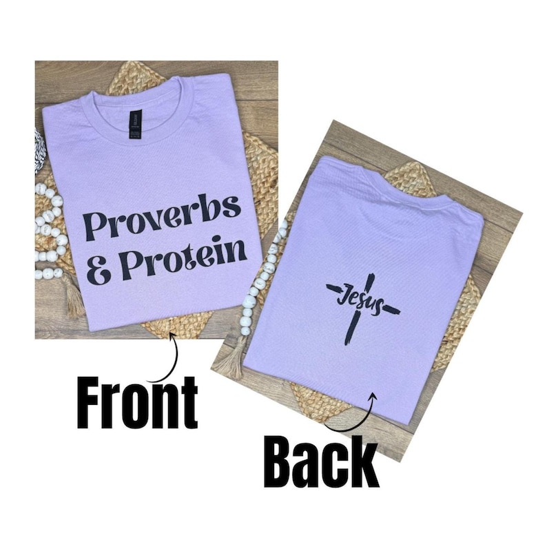 May include: A lilac t-shirt with the text "Proverbs & Protein" on the front. The back of the shirt features a cross with the word "Jesus" underneath. The shirt is displayed on a woven mat.