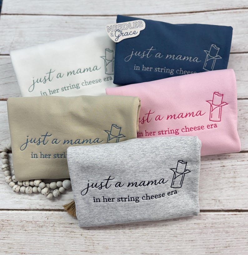 May include: Five folded sweatshirts in various colors: white, navy blue, pink, tan, and gray. Each sweatshirt has the embroidered text "just a mama in her string cheese era" with a string cheese graphic.