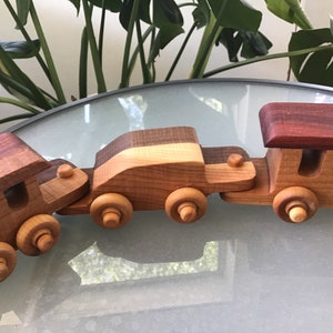 May include: A wooden toy train set with a locomotive, a car, and a boxcar. The train is made of different types of wood, including cherry, maple, and walnut. The train is painted in natural wood tones.