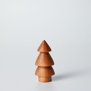 May include: A wooden Christmas tree ornament with three tiers. The tree is a light brown color and has a smooth finish.