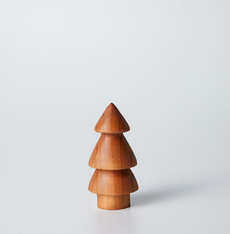 May include: A wooden Christmas tree ornament with three tiers. The tree is a light brown color and has a smooth finish.