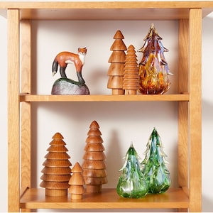 May include: A wooden shelf with a variety of wooden and glass Christmas tree ornaments. The ornaments are arranged in a staggered pattern on the shelf. There is a wooden fox figurine on the top shelf.