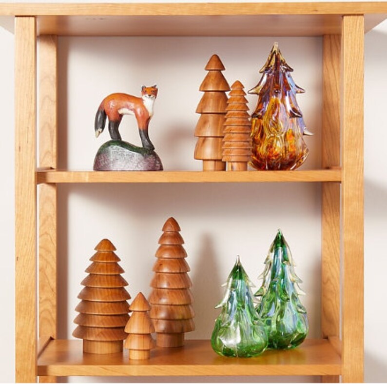May include: A wooden shelf with a variety of wooden and glass Christmas tree ornaments. The ornaments are arranged in a staggered pattern on the shelf. There is a wooden fox figurine on the top shelf.