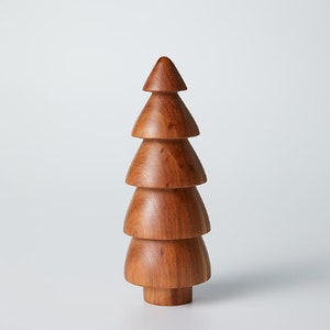 May include: A wooden Christmas tree ornament with a brown finish. The tree is made of stacked, tiered pieces of wood.