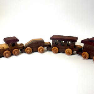 May include: A wooden toy train set with four cars, including a locomotive with the name "Cooper" engraved on the side. The train is made of dark wood with brown and light brown accents.