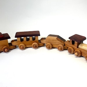 May include: A wooden toy train set with a brown engine, a brown caboose, a brown passenger car, and a wooden flatbed car. The train is made of natural wood with a dark brown stain.