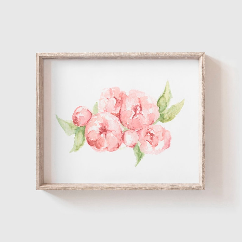 May include: Watercolor painting of pink peonies with green leaves, set in a light wood frame. The floral artwork features soft, delicate brushstrokes and a white background. A decorative piece for home decor.