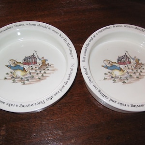 Puede incluir: Dos cuencos de cerámica blanca con una ilustración azul y blanca de un conejo corriendo de un hombre con un rastrillo. El texto alrededor del borde de los cuencos dice "Stop thief! But round the end of a cucumber frame, whom should he meet but Mr. McGregor! he jumped up and ran after Peter waving a rake and calling out, Stop thief!"