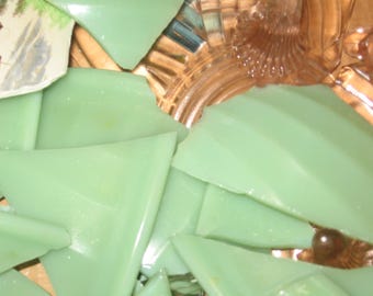 May include: A close-up of a pile of broken green glass pieces. The glass is translucent and has a slightly cloudy appearance. The pieces are arranged in a random pattern.