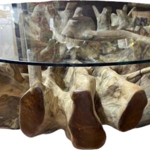 May include: A unique coffee table featuring a clear, round glass top supported by a base crafted from natural, light-brown wood. The base has an organic, sculptural design, showcasing the wood's natural grain and texture. The table's design is modern and artistic.