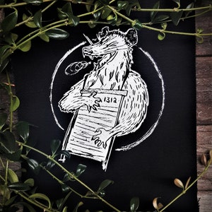 May include: Black and white embroidered patch depicting a cartoon possum holding a scroll with the number "1312" written on it. The possum is wearing a bow tie and has a mischievous expression.