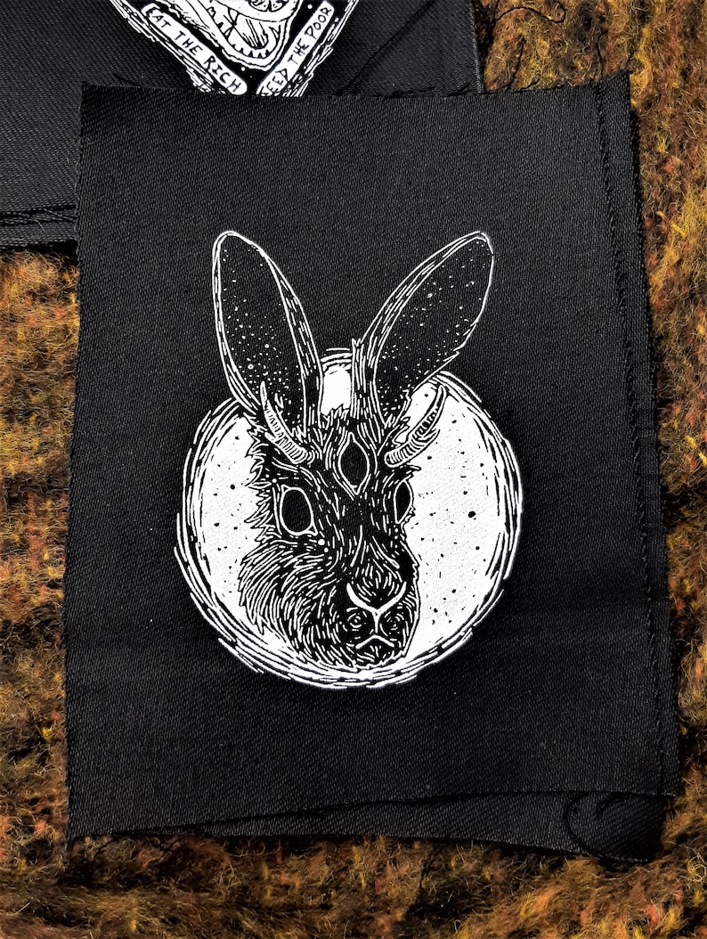May include: Black and white illustration of a rabbit with four eyes, printed on a black fabric patch.