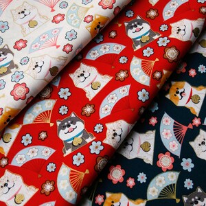 Puede incluir: Tela con un patr&oacute;n repetido de perros Shiba Inu, abanicos y flores en rojo, blanco y azul marino. Los perros tienen diferentes colores y llevan collares. Los abanicos son de color azul claro y dorado, y las flores son rosas y blancas.