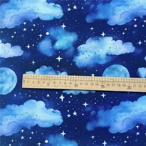 May include: Blue fabric with a watercolor pattern of white clouds and stars on a dark blue background. A ruler is placed on the fabric, with the numbers 1 through 22 visible.