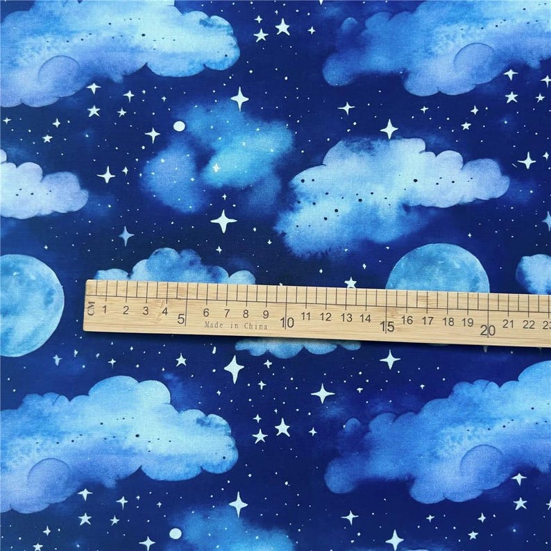 May include: Blue fabric with a watercolor pattern of white clouds and stars on a dark blue background. A ruler is placed on the fabric, with the numbers 1 through 22 visible.