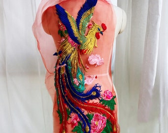 May include: A large, colorful embroidered patch featuring a phoenix with a long, flowing tail. The phoenix is gold, red, blue, and green, and is surrounded by pink and green flowers. The patch is perfect for adding a touch of whimsy to clothing or accessories.