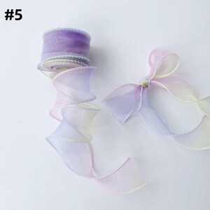 May include: A roll of sheer, ombre ribbon in shades of purple, pink, and yellow. The ribbon is partially unrolled, revealing a spiraling design. A tied bow made of the same ribbon is also visible. The text "#5" is in the upper left corner.