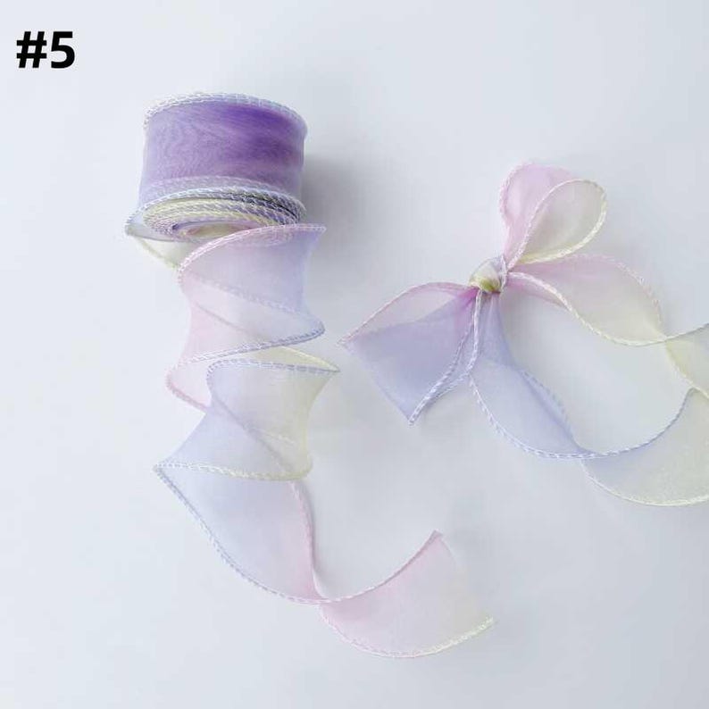 May include: A roll of sheer, ombre ribbon in shades of purple, pink, and yellow. The ribbon is partially unrolled, revealing a spiraling design. A tied bow made of the same ribbon is also visible. The text "#5" is in the upper left corner.