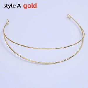 May include: A gold-colored necklace with a double-layered design. The necklace is made of thin, curved metal and features the text "style A gold" in the upper left corner. The necklace is displayed on a white background.