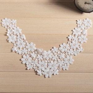 Pode incluir: Colete de renda branca com um delicado padrão floral. O colar é feito de um tecido macio e leve, perfeito para adicionar um toque de elegância a qualquer roupa.