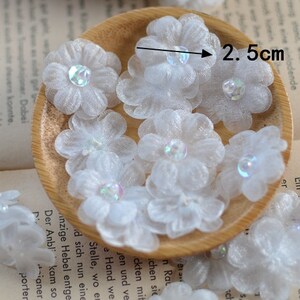May include: A close-up of a wooden bowl filled with white tulle flowers, each with a iridescent center. The flowers are approximately 2.5 cm in diameter.