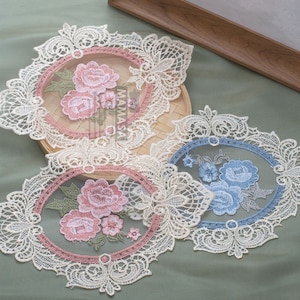 May include: Three white lace doilies with embroidered floral designs. The doilies feature pink, blue, and green floral patterns.