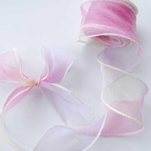 May include: A roll of sheer pink and white ribbon with a delicate white trim. A bow made from the same ribbon is also visible. The ribbon is ideal for gift wrapping, crafting, or adding a touch of elegance to any project.
