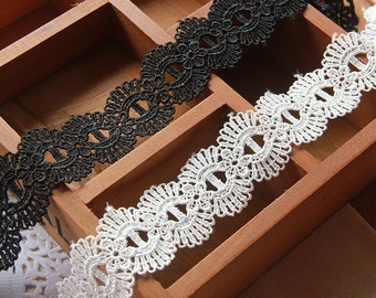 Puede incluir: Primer plano de un ribete de encaje negro y blanco con un diseño floral. El encaje se muestra en una caja de madera, mostrando sus intrincados patrones y texturas. Ideal para coser, hacer manualidades o añadir un toque delicado.