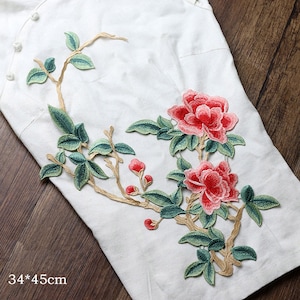 Könnte beinhalten: Ein floraler Stickerei-Patch mit zwei rosa und roten Blumen und grünen Blättern auf einem weißen Stoffhintergrund. Der Patch misst 34 mal 45 Zentimeter.